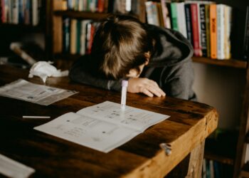 boy in gray hoodie reading book on brown wooden table