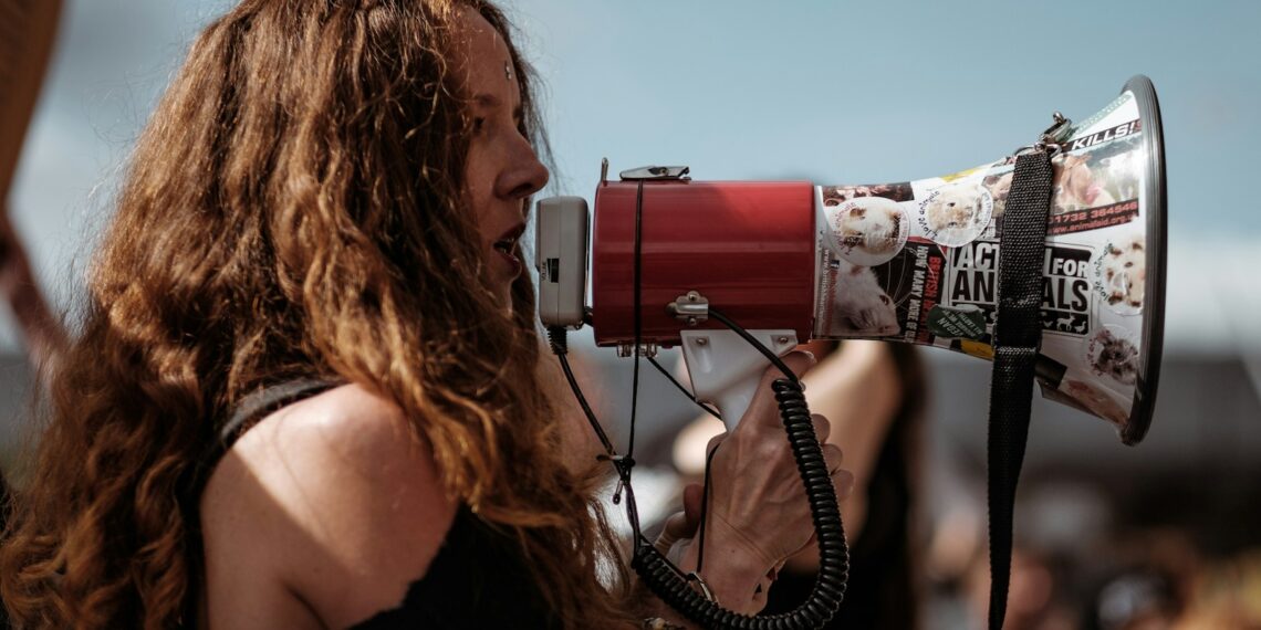 selective focus photography of woman wearing black cold-shoulder shirt using megaphone during daytime
