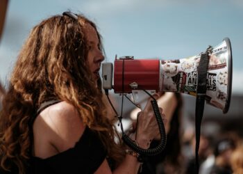 selective focus photography of woman wearing black cold-shoulder shirt using megaphone during daytime
