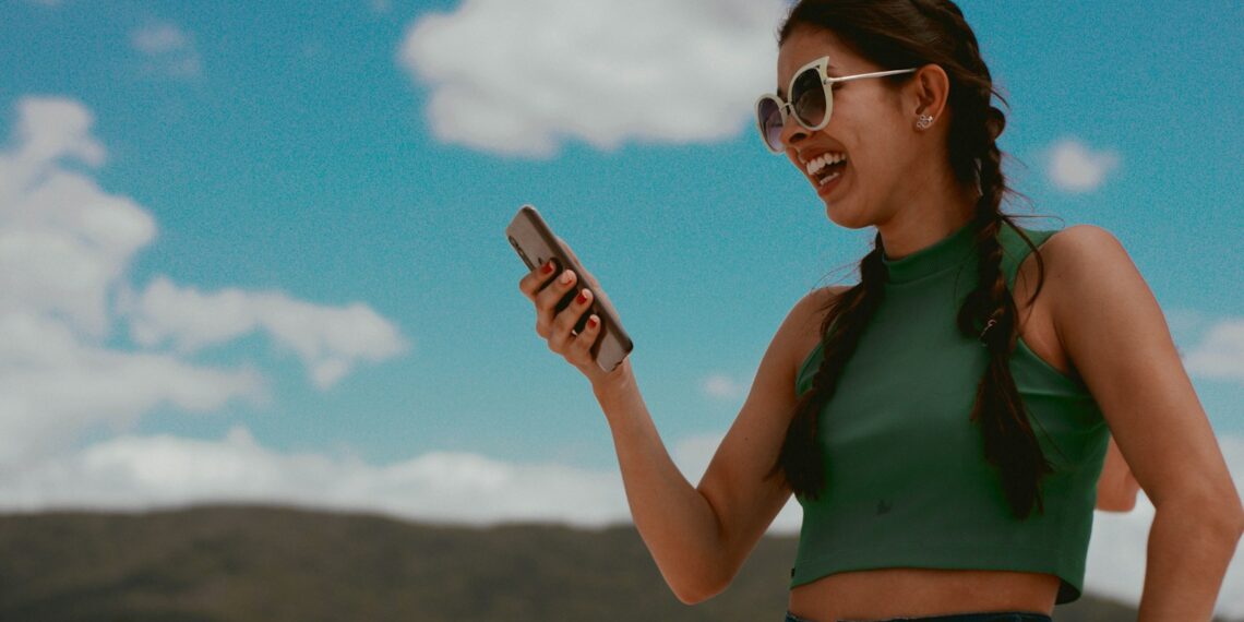 woman in green tank top holding smartphone during daytime