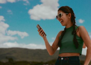 woman in green tank top holding smartphone during daytime