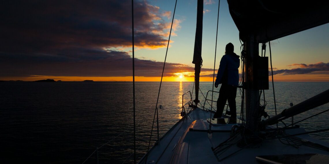 a person standing on the deck of a boat at sunset
