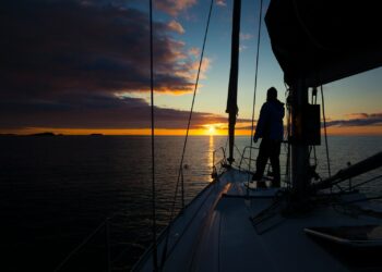 a person standing on the deck of a boat at sunset
